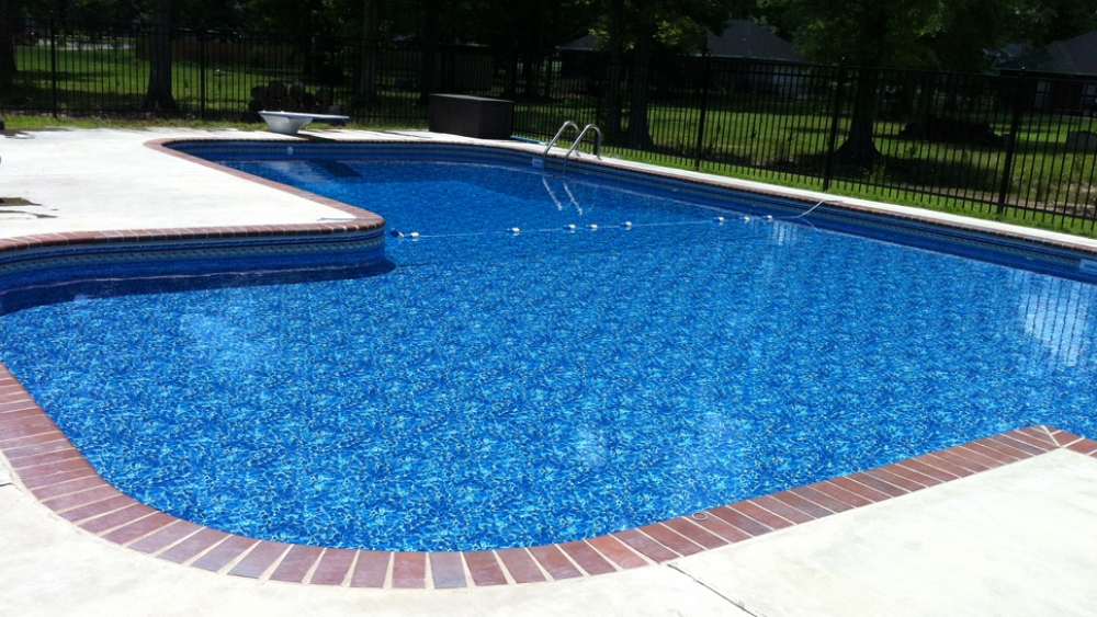 L-shaped pool with a beautiful blue pool liner, brick coping and a diving board.
