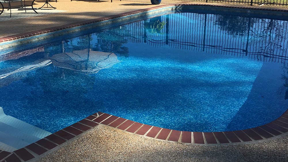 Relaxing blue lined pool with brick coping and an aggregate concrete pool deck.